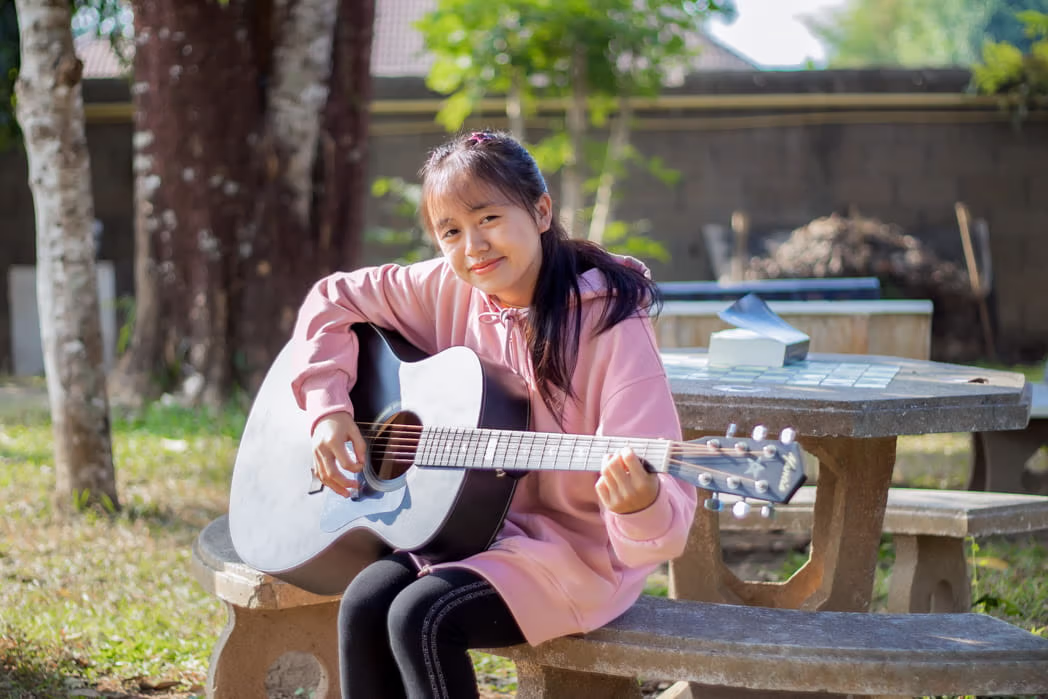 Young girl sitting on a bench playing a guitar.