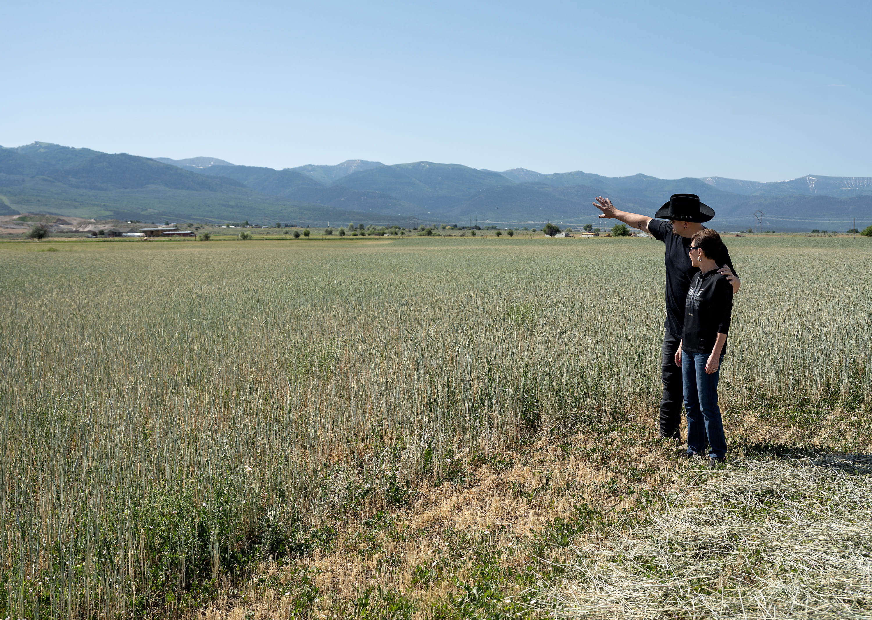 Two people standing in a wide open field, one pointing toward distant mountains.