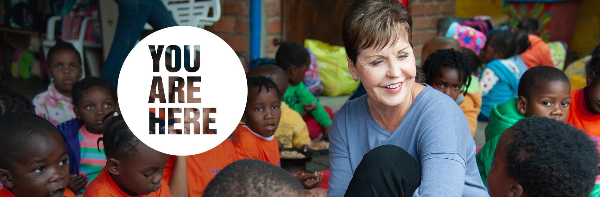 A diverse group of children sitting in a crowded room, with a large circular inset graphic in the center that reads "YOU ARE HERE."