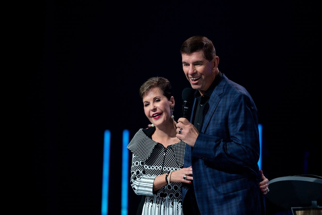 Dave and Joyce Meyer on stage smiling and speaking at a conference