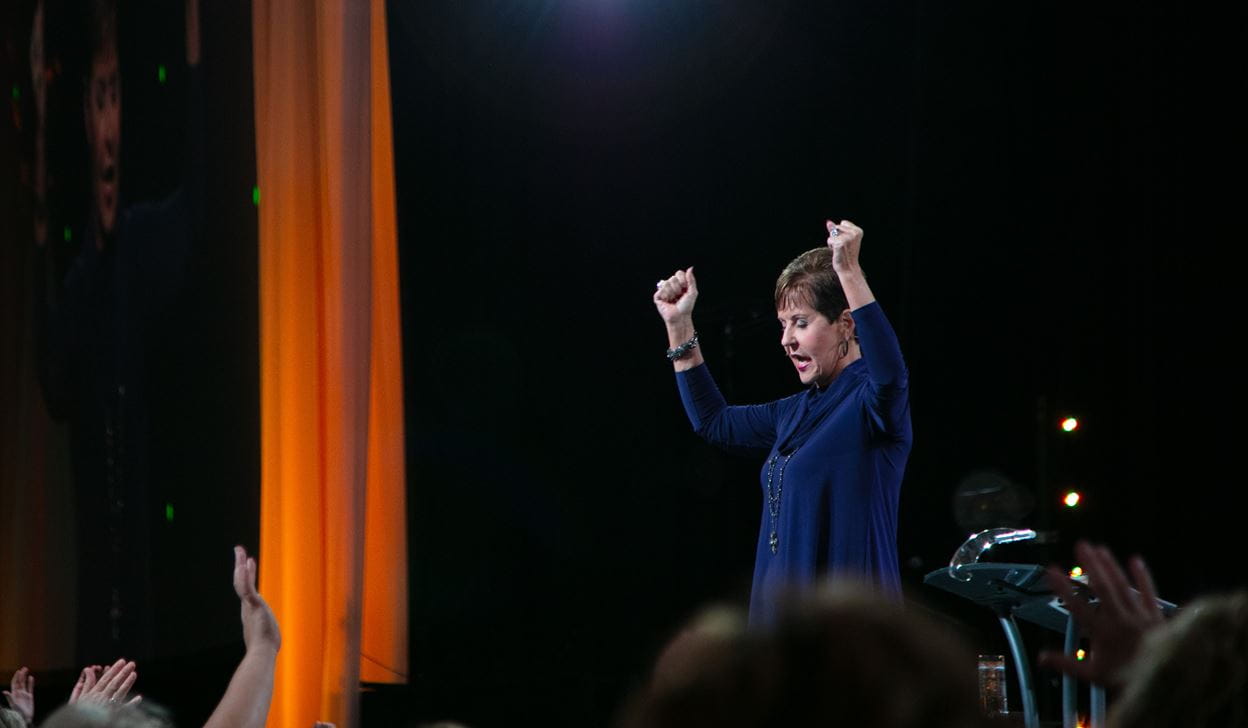 Joyce Meyer praying on stage at a live conference.