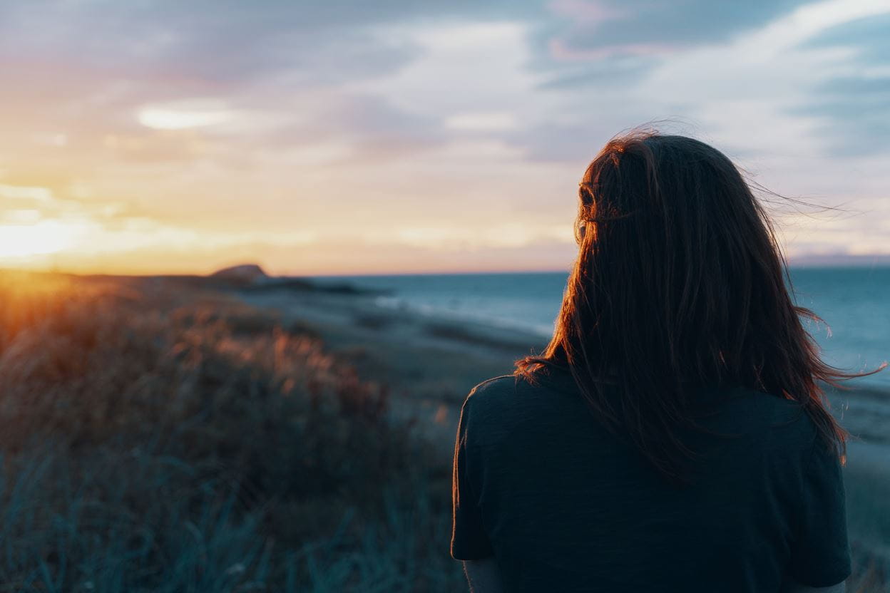 Image of a woman looking at a serene ocean sunset.