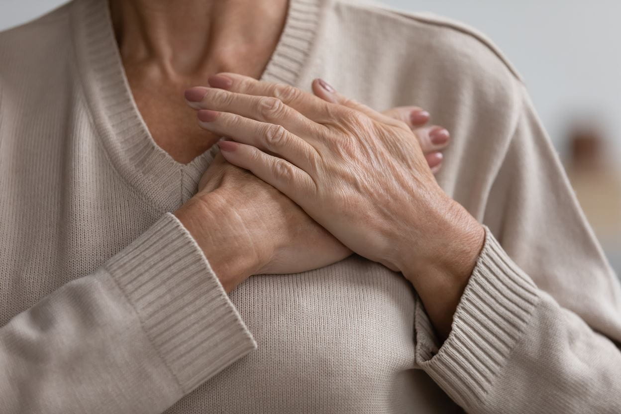 A close view of a woman holding her folded hands over her heart.