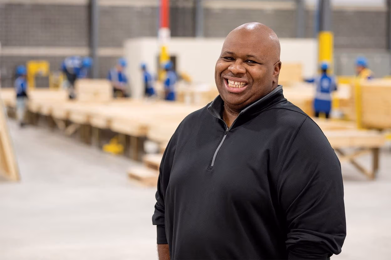 Amin Irving smiling in a warehouse with people working in the background
