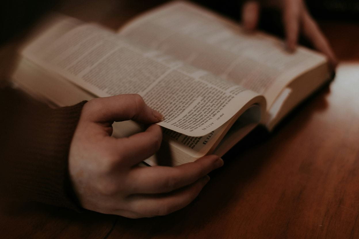 A woman's hands holding open a Bible on a desk reading a daily devotional.