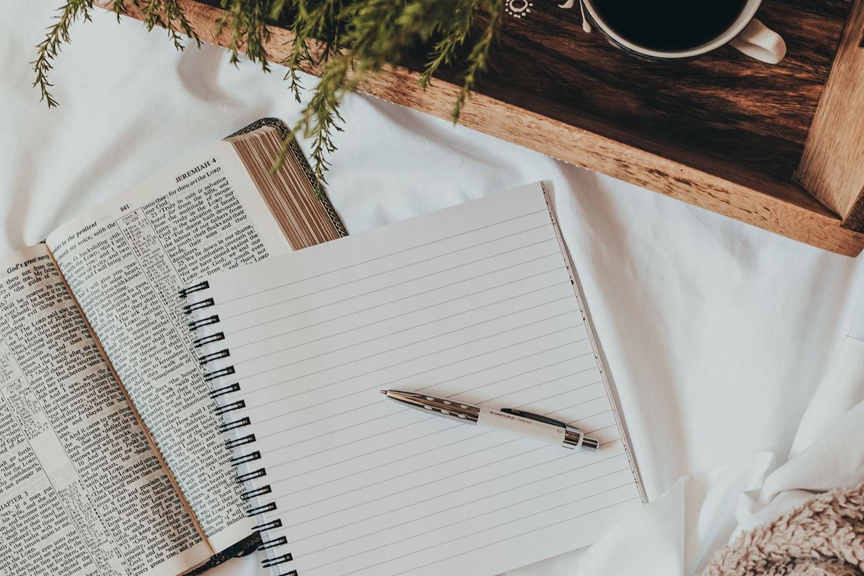 An open Bible and journal on a sheet ready for reading a daily devotional.