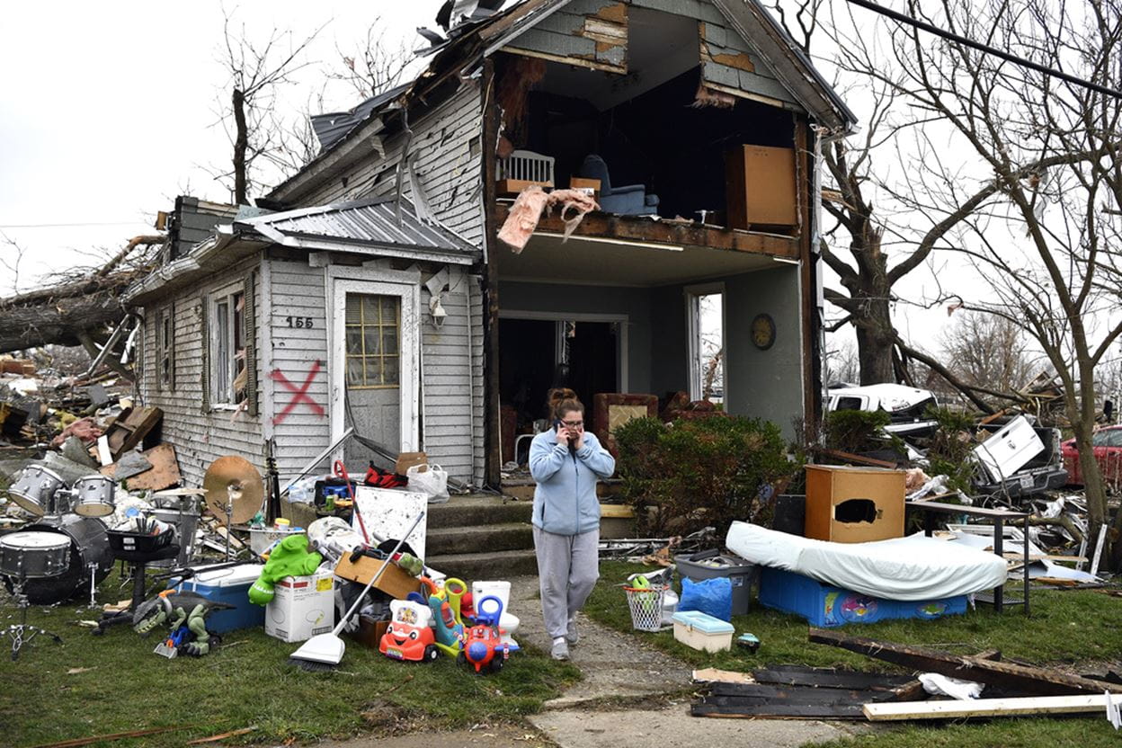 Woman on the phone in front of a Storm destroyed house