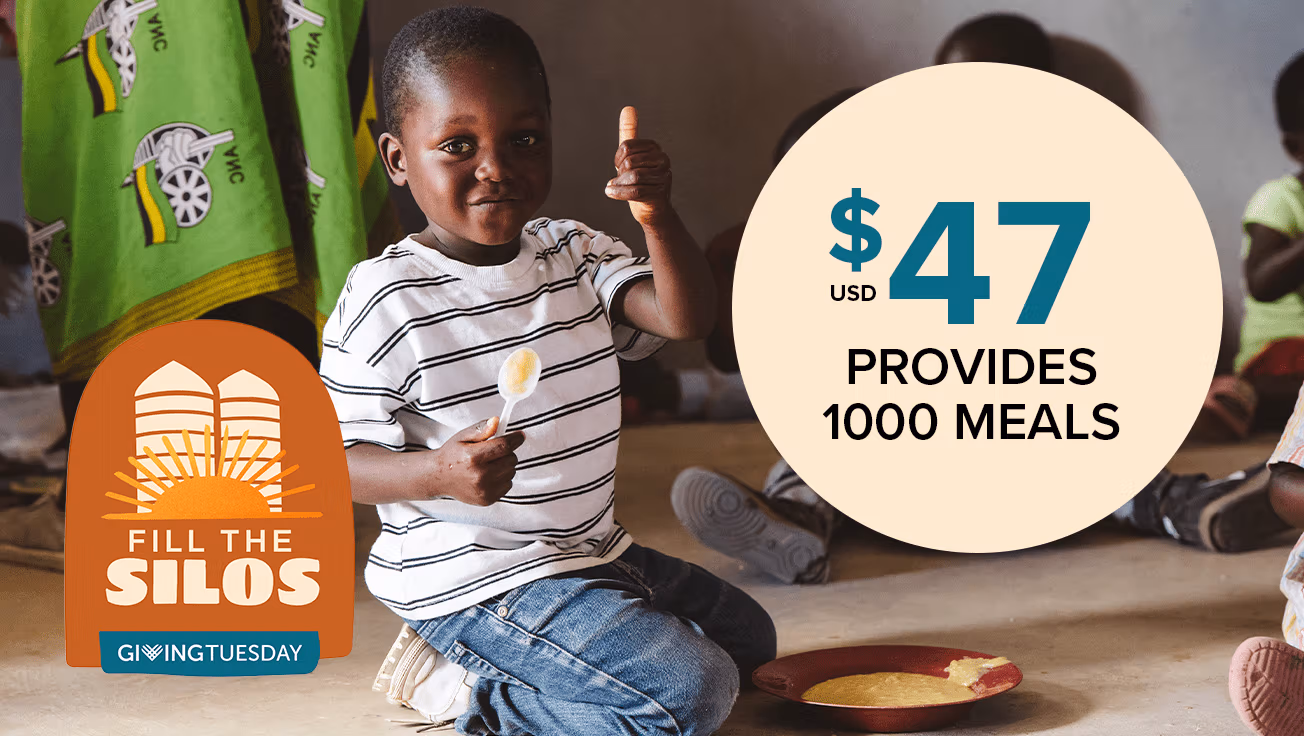 A boy with a plate of food holding a thumbs up.