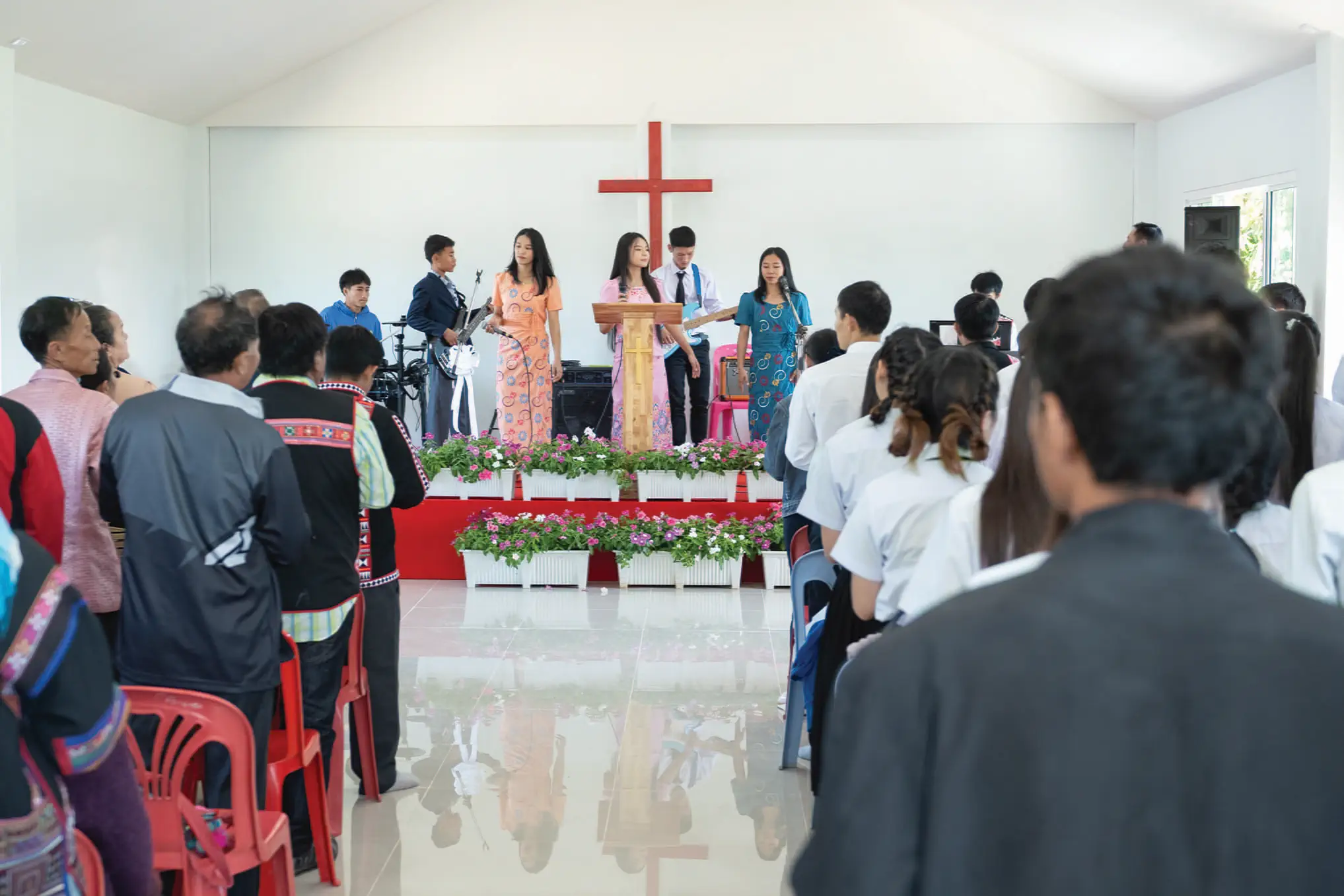 Church congregation standing during a worship service with singers and musicians on stage beneath a cross.