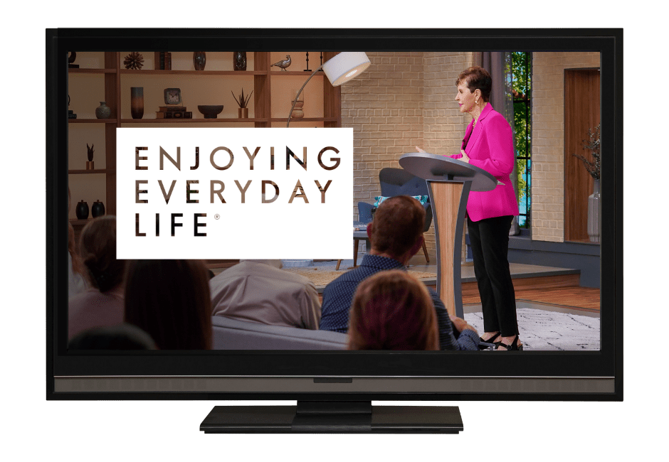 Television screen displaying 'Enjoying Everyday Life' with a speaker in a bright pink outfit addressing an audience in a modern studio setting